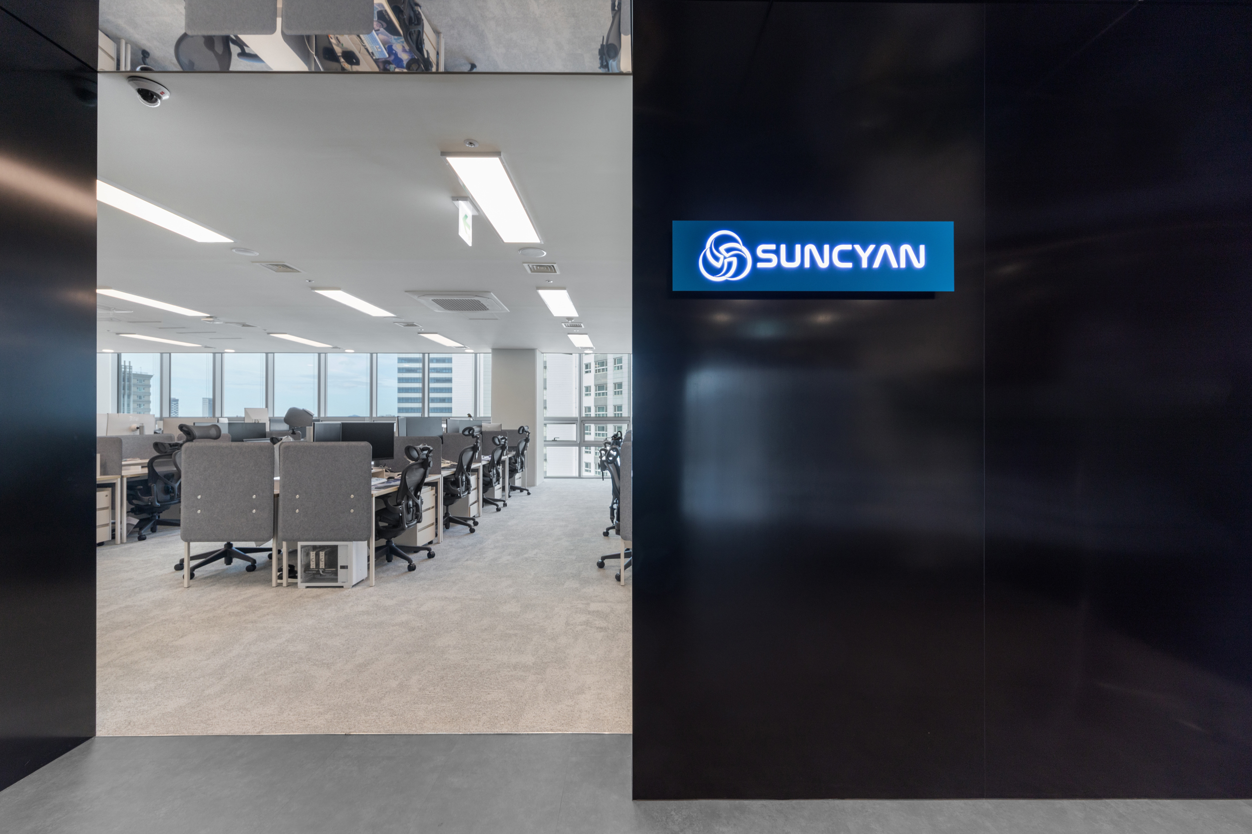 선시안 SUNCYAN 오피스 입구 인테리어, 블랙 메탈 벽면의 블루 발광 로고와 오픈형 업무공간이 연결된 진입 공간, 공간 디자인 그룹 시드나인 SIDnine 설계·시공